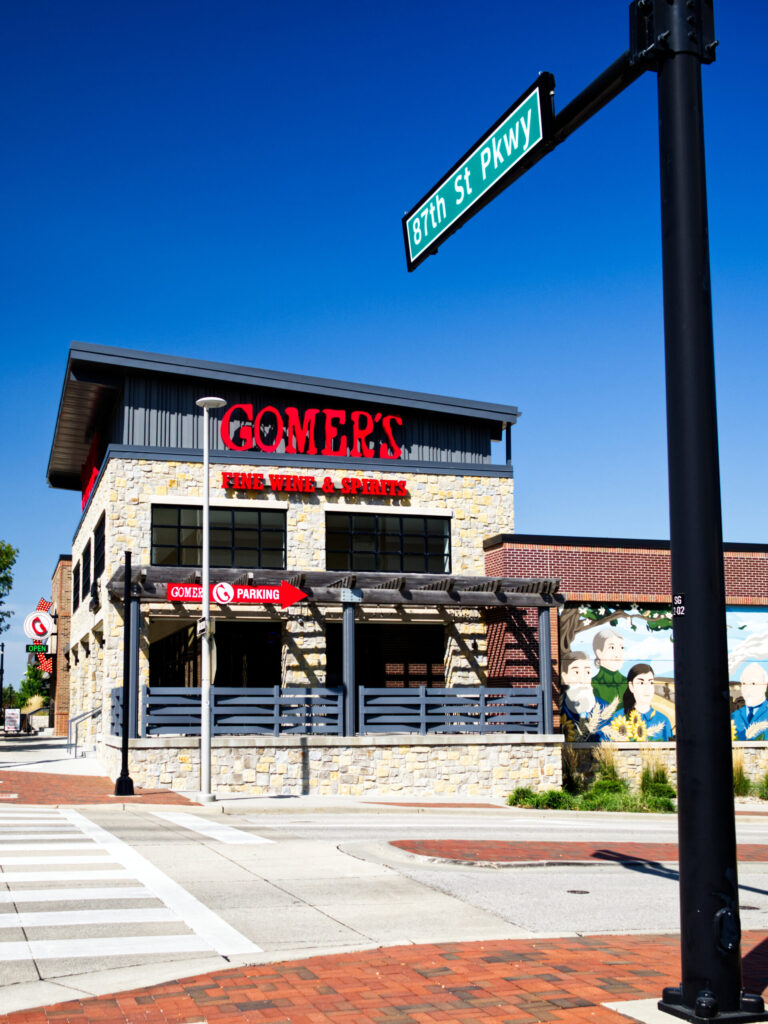 An image of a liquor store seated at the corner of an intersection with a street sign in the foreground.